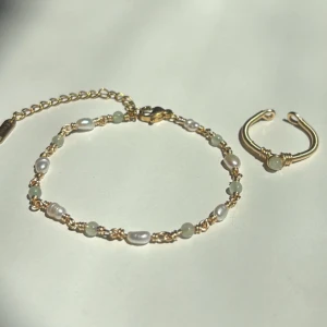 New Jade Set - Setet innehåller: ✓ Ett handgjort armband ✓ En justerbar ring  Armband: Längd: 16,5 cm + 6,5 cm förlängningskedja Material: Rostfritt stål, äkta sötvattenspärlor och New Jade (ädelsten)  Ring: Justerbar storlek Material: Rostfritt stål med äkta New Jade (ädelsten)