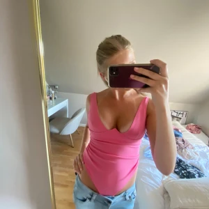 Rosa bodysuit från NLY One - Säljer en rosa body från NLY One med djup v- ringning. Är perfekt att styla med jeans eller kjol. Materialet är stretchigt och mjukt, vilket gör den superbekväm och snygg. Aldrig använd🩷