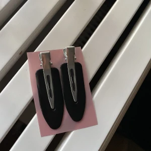 Svarta hårklämmor i metall - Två stilrena svarta hårklämmor med silvriga metalldetaljer. Perfekta för att hålla håret på plats eller som en snygg accessoar till din frisyr. Klämmorna har en klassisk form och är lätta att använda. Eller om man vill sätta upp håret när man sminkar sig!