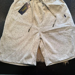 Grå shorts från Polo Ralph Lauren - Snygga grå shorts från Polo Ralph Lauren med klassisk broderad logga på benet. Mjukt bomullsmaterial och bekväm passform med snörning i midjan. Perfekta för chill dagar eller när du vill ha en clean och enkel stil.