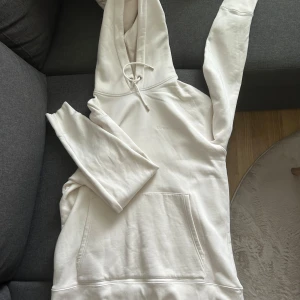 Vit hoodie från J.Lindeberg - Snygg vit hoodie från J.Lindeberg med broderad logga på bröstet. Tröjan har huva med snörning, känguruficka och långa ärmar. 100% bomull. Liten fläck på kanten men går säkert att få bort med lite medel. Använd några fåtal gånger men annars inga defekter.