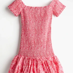Rosa offshoulder kortklänning - Superfin rosa kortklänning med offshoulder och korta ärmar. Klänningen har ett vitt mönster, smockad överdel och volangig kjol. Perfekt för sommarens alla tillfällen och ger en riktigt söt vibe.