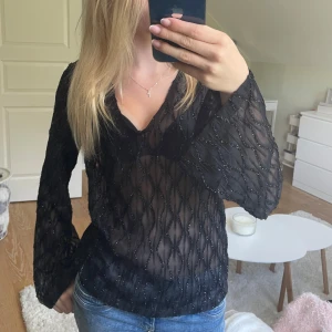 Svart  blus från Vila - Säljer en svart transparent blus från Vila i storlek 34. Blusen har ett vågigt mönster med glittriga detaljer och v-ringning. Långa ärmar och lätt, luftig känsla. Perfekt för dig som vill sticka ut med en snygg och trendig topp.    Endast använd enstaka gån, säljer då den bara hänger i garderoben 💓
