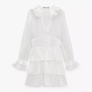 Vit volangklänning från Zara - Supersöt vit kortklänning från Zara med volanger, långärmade ärmar och broderad krage. Klänningen har knappar framtill. Köptes för 499 kr! Endast använd en gång