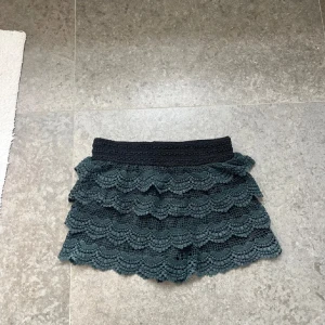 Mörkgrön volangkjol med spets - Supersöta mörkgröna shorts  med flera lager volanger och spetsdetaljer. Resår i midjan för skön passform. Perfekt för dig som gillar en lekfull och trendig stil.