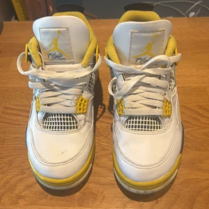 Nike Air Jordan 4 Retro Tour Yellow - Nike Air Jordan 4 Retro Tour Yellow med vit ovandel i skinn, svarta och gula detaljer samt meshpaneler. Klassisk Jumpman-logga på plös och häl, gul vadderad insida och snörning framtill. Snygg kontrast mellan svart, vitt och gult gör dessa sneakers till ett statement.