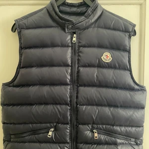 Moncler Gui vest - En moncler GUI väst. Västen är i ett mycket gott skick, den är använd bara ett fåtal gånger. Säljer denna väst då jag har vuxit ur den. Västen är en storlek S och är i färgen mörkblå. NFC fungerar perfekt och den Scannar till moncler sidan. Kom priv för mer info, frågor och även mer bilder om det önskas. 