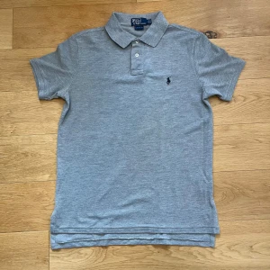 Polo Ralph Lauren Piké - Klassisk grå pikétröja från Polo Ralph Lauren. Tillverkad i mjuk bomull och har en clean, stilren look som funkar till allt. Den är sparsamt använd då den endast har används vid finare tillfällen.