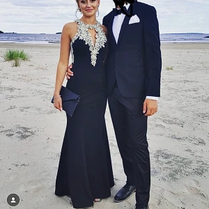 Svart långklänning med vackra detaljer - Svart långklänning med öppen rygg och silvrigt blommönster med pärlor. Perfekt för festliga tillfällen. Detaljerna framtill, längs ryggen och det extremt sköna materialet ger en super lyxig känsla. Storlek S, material: 100% polyester. Jag är 168 cm lång och klänningen är sydd för att passa mig med klackar. Använt vid två tillfällen. Köpte klänningen för 5000kr, säljer den för 3000kr.