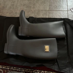 Svarta höga stövlar från NIBU - Snygga svarta höga stövlar från NIBU med stilren design och guldfärgad metallplatta framtill på skaftet. Stövlarna har rund tå och platt sula, tillverkade i syntetmaterial som ger en clean och modern look. 250kr. Aldrig använda 