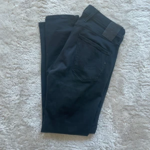 Svarta Replay Anbass jeans herr - Svarta Replay Anbass jeans i stretchigt Hyperflex-material. Klassisk femficksmodell med dragkedjegylf och Replay-logga på fickan. Snygg, smal passform och stilren look som funkar till allt. Perfekta för dig som gillar bekväma och moderna jeans.