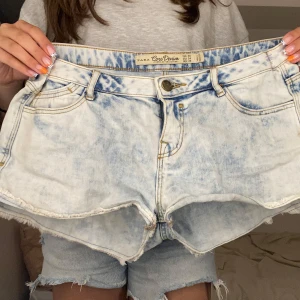 Ljusblå jeansshorts från Zara - Säljer ett par ljusblå, acid wash jeansshorts från Zara med fransig kant och klassisk femficksmodell. Shortsen har hög midja och coola slitningar för en avslappnad vibe. Perfekta till sommaren och lätta att matcha med allt.