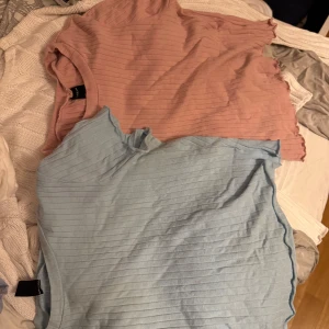 2 ribbade toppar från SHEIN, S - Två snygga ribbade toppar från SHEIN i storlek S. En är ljusblå och den andra är ljusrosa, båda med kort ärm och vågig kant vid ärmslut och nederkant. Perfekta att matcha med jeans eller kjol för en chill look.