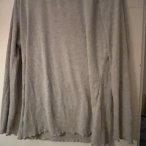 Ljusgrå långärmad tröja ISABEL - Ljusgrå långärmad tröja från ISABEL med enkel och clean look. Tröjan har en rak passform och är tillverkad i mjukt material, perfekt för lager-på-lager. Fint vågig kant nertill ger en extra detalj.