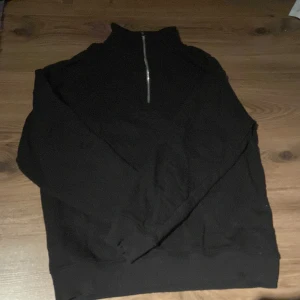 Svart half zip tröja från 157 - Svart långärmad tröja från 157 med halv dragkedja och hög krage. Enkel och stilren design, perfekt för lager-på-lager. Mjuk och skön känsla, passar dig som gillar basic och clean look.