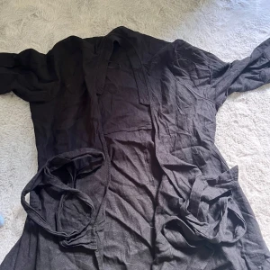 Svart långkofta från Lindex - Svart långkofta från Lindex i storlek L. Koftan har omlottmodell med knytband i midjan och långa ärmar. 
