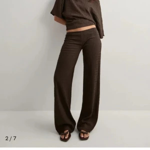 Bruna low waist byxor från Nelly - Snygga bruna byxor från Nelly med låg midja och strukturerat tyg. Vida ben ger en chill och trendig look. Perfekta att styla med crop top eller oversized skjorta. Materialet känns mjukt och har en cool textur som sticker ut.