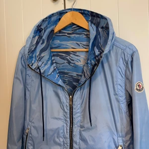 Moncler reversible windbreaker - Moncler windbreaker i modellen Gobert med babyblå färg på utsidan och blått camo insidan. Sällsynt jacka som inte sålts på länge. Vändbar så man kan ha jackan ut och in där loggan på armen syns på båda sidor. Storlek 3 och skicket är som ny, endast pyttesmå repor men det syns inte om man inte kollar väldigt noga