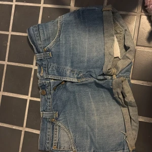 Blå jeansshorts med knyt från Lee - Snygga blå jeansshorts från Lee med klassisk femficksdesign och knytband i midjan. Shortsen har Lee-logga på bakfickan och slitna detaljer för en cool look. Perfekta för varma dagar när du vill ha en avslappnad stil.