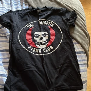 Svart Misfits Fiend Club t-shirt - Svart t-shirt från Bandmerch med stort Misfits Fiend Club-tryck på bröstet. Klassisk rund hals, korta ärmar och rak passform. Tillverkad i 100% bomull, perfekt för dig som gillar bandmerch och punkstil. Super skön tröja!💞