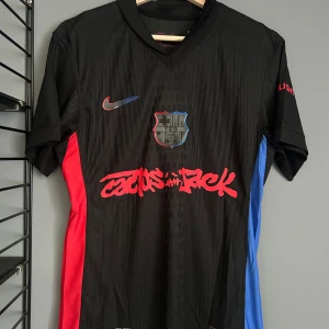 FC Barcelona Lamine Yamal tröja Nike - Snygg svart FC Barcelona fotbollströja från Nike med Lamine Yamal och nummer 19 på ryggen. Tröjan har röda och blå detaljer på sidorna, klubbmärke på bröstet och coolt rödtryck framtill. Kortärmad och tillverkad i lätt, ventilerande material.helt ny med tagg en replika 