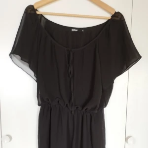 Svart kortklänning från Cubus - Svart blus eller kortklänning från Cubus i luftig och transparent polyester. Den har vida, korta ärmar, resår i midjan och knytning framtill. Perfekt för dig som gillar en enkel men snygg look med flowy känsla. Storleken är 34 men eftersom den är flowy passar den även stl 36 och 38.