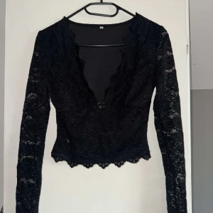 Svart spetsblus - Säljer en svart blus i spets med lång ärm och djup v-ringning. Blusen har fina spetsdetaljer. Säljer den då den är lite stor runt bystet. Andvänd en gång💕