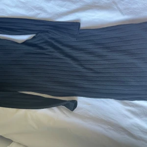 Svart ribbad långärmad klänning - Säljer en svart ribbad långärmad klänning i stretchigt material. Klänningen har en kroppsnära passform och är perfekt för dig som gillar en stilren och enkel look. Längden är mellan knä och vad. Passar till många olika tillfällen.