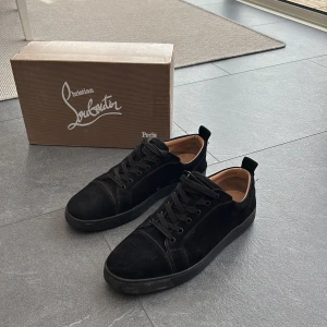 Svarta sneakers från Christian Louboutin - Säljer ett par svarta sneakers från Christian Louboutin i mocka med klassisk röd sula. Skorna har rund tå, svarta skosnören och diskret branding. Perfekta för dig som vill ha något stilrent men ändå lyxigt. Säljes då jag är sugen på ett par andra skor.