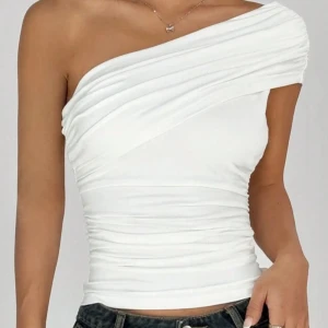 Vit one shoulder topp - Säljer en snygg vit one shoulder topp med draperad design. Toppen är tight och har en stilren look som passar perfekt till jeans eller kjol. Perfekt för dig som vill sticka ut lite extra!