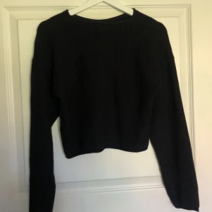 Svart stickad croppad tröja från Uniq Young - En svart stickad tröja från Uniq Young i croppad modell. Tröjan har rund halsringning och långa ärmar. Perfekt för dig som gillar en enkel och stilren look med lite kortare passform.