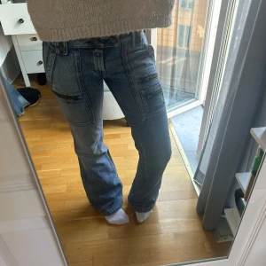 Blå bootcut jeans med dragkedjedetaljer - Säljer ett par blå bootcut jeans från Replay med flera dragkedjor framtill och på bakfickan. 