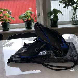 Nike Zoom Mercurial Elite fotbollsskor svart/blå - Säljer ett par Nike Zoom Mercurial fotbollsskor i svart med blå och vita detaljer. Skorna har snörning, låg profil och är designade för optimal prestanda på planen. Perfekta för dig som vill ha lätta och snabba skor med bra grepp.
