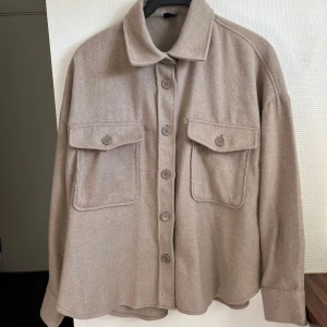 Tunn tygkappa Gina Tricot - Säljer en beige tunn tygkappa från Gina tricot i storlek M