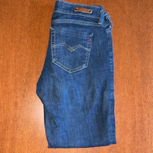 Blå jeansbyxor från Replay - Säljer ett par klassiska blå jeansbyxor från Replay  med snygga detaljer på bakfickorna. Byxorna har normal passform och är tillverkade i ett slitstarkt denimtyg. Perfekta för dig som gillar tidlös stil och bra kvalitet.