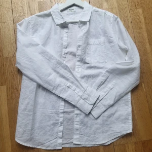 Vit linneskjorta i nytt skick - Säljer en klassisk vit skjorta i linne i nytt skick. Snygg att bära både öppen och knäppt till sommaren. Storleken är 170, men den är lite större än så och passar ca 170-180. Priset är inte satt i sten, så kontakta gärna! 