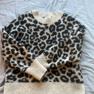 Leopardmönstrad stickad tröja från & Other Stories - Säljer en supermjuk stickad tröja från & Other Stories med leopardmönster i svart och beige. Tröjan har rund halsringning, långa ärmar och breda ribbade muddar vid ärmslut och nederkant. Perfekt för dig som vill sticka ut lite extra!