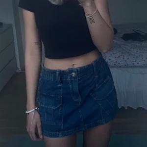 Blå jeanskjol från BDG Urban Outfitters - Säljer en blå jeanskjol från BDG Urban Outfitters i storlek XS. Kjolen har två stora fickor framtill, resår i midjan och stängs med dragkedja och knapp. 