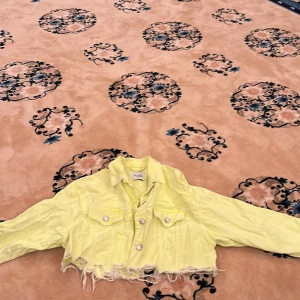 Gul croppad jeansjacka från Zara - Säljer en ljusgul croppad jeansjacka från Zara med fransad nederkant och klassisk krage. Jackan har två bröstfickor med knappar och silverfärgade detaljer. Perfekt för dig som vill sticka ut med färg.