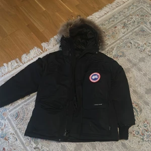Svart dunjacka från Canada Goose med pälskant 🙂 - Säljer en svart Canada Goose dunjacka med huva och pälskant. Jackan har dragkedja, flera fickor och den klassiska Canada Goose-loggan på ärmen. Perfekt för på kalla dagar och riktigt varm.