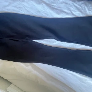 Svarta kostymbyxor från Gina tricot - Svarta kostymbyxor från Gina tricot i klassisk modell med två knappar och dragkedja framtill. Byxorna har raka ben och fickor med lock och knapp bak. Perfekta för en stilren look.