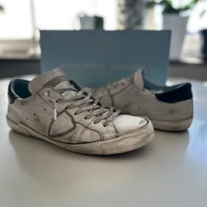 Vita sneakers från Philippe Model - Säljer ett par vita Philippe Model sneakers med grå detaljer och svart häl. Klassisk låg modell med snörning och rund tå. Skorna har en platt sula och är tillverkade i skinn. Perfekta för dig som gillar stilrena och tidlösa sneakers. Dem är lite slitna och smutsiga(kan nog lätt tvättas bort) skorna har ett litet slitage på sulan. Skick 6/10 nypris 2600kr mitt pris 999kr