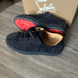 Mörkblåa sneakers från Christian Louboutin - Säljer ett par svarta sneakers i mocka från Christian Louboutin med ikoniska röda sulor och svarta nitar över hela tån. Saknas 1 nit på vardera sko men det är inget som märks. Riktigt stilrena skor som jag rekommenderar för den som vill vara lite extra uppklädd💯💯skicka en chat vid frågor😊👍