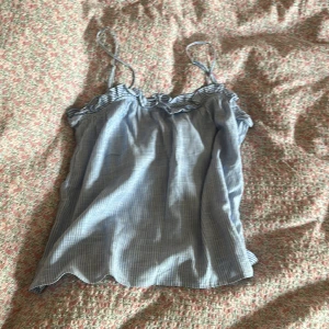 Blå- och vitrandig linnetopp med volang - Säljer en söt blå- och vitrandig linnetopp med tunna justerbara axelband och volangdetalj upptill. Toppen är luftig och har en avslappnad passform, och är perfekt för sommaren. Linnet passar folk med olika storlekar men självaste toppen är storlek S men passar också bra på personerna med storleken M och Xs