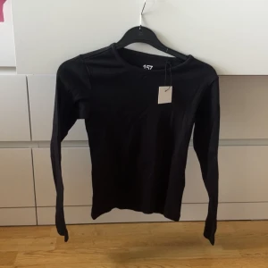 Svart ribbad långärmad tröja från 157 - Svart långärmad tröja från 157 i ribbat material. Enkel och stilren modell med rund halsringning, perfekt för lager-på-lager eller som basplagg. Snygg och bekväm för vardagslooken.