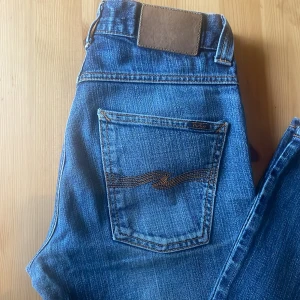 Blå jeansbyxor från nudie - Klassiska blå jeansbyxor från nudie med raka ben och normal passform. Jeansen har fem fickor, dragkedja och knapp framtill samt diskret logga på bakfickan. Perfekta till vardags och enkla att matcha. Jeansen har L32 och W29