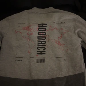 Hoodrich Mjukisset – Grå - Säljer detta snygga och bekväma mjukisset från Hoodrich. Setet består av en sweatshirt och matchande byxor i ljusgrå färg med mörkgrå detaljer. Båda delarna har Hoodrich-loggan tryckt, och byxorna har dragkedjefickor för extra funktionalitet. Använt men i fint skick – perfekt för vardag eller chill.