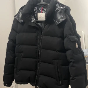 Moncler montgenevre jacka  - Säljer en svart pufferjacka från Moncler med huva och dragkedja. Jackan har quiltad design, ficka med lock och Moncler-logga på ärmen. Perfekt för kalla dagar och riktigt snygg streetstil storlek 1 passar som storlek 2 .