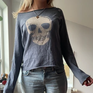 Grå tröja med döskalle från Zadig & Voltaire - Säljer en grå/blå långärmad tröja från Zadig & Voltaire med en stor beige döskalle framtill. Tröjan har en avslappnad passform och är perfekt för dig som gillar edgy detaljer. Superenkel att styla till jeans eller kjol.