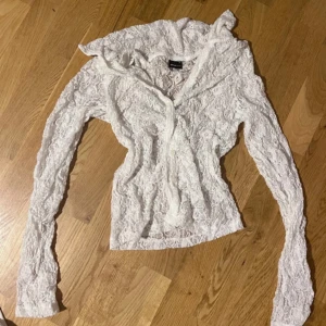 Vit spetstopp  med knappar - Säljer en tunn och feminin vit topp i spets med långa ärmar och knappar framtill. Perfekt för lager-på-lager och ger en romantisk touch till outfiten. Snygg att styla över ett linne eller klänning. Tajt passform mycket fin.